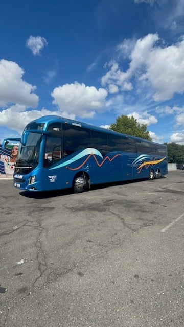 Blue and white coach bus parked on asphalt under blue sky with white clouds